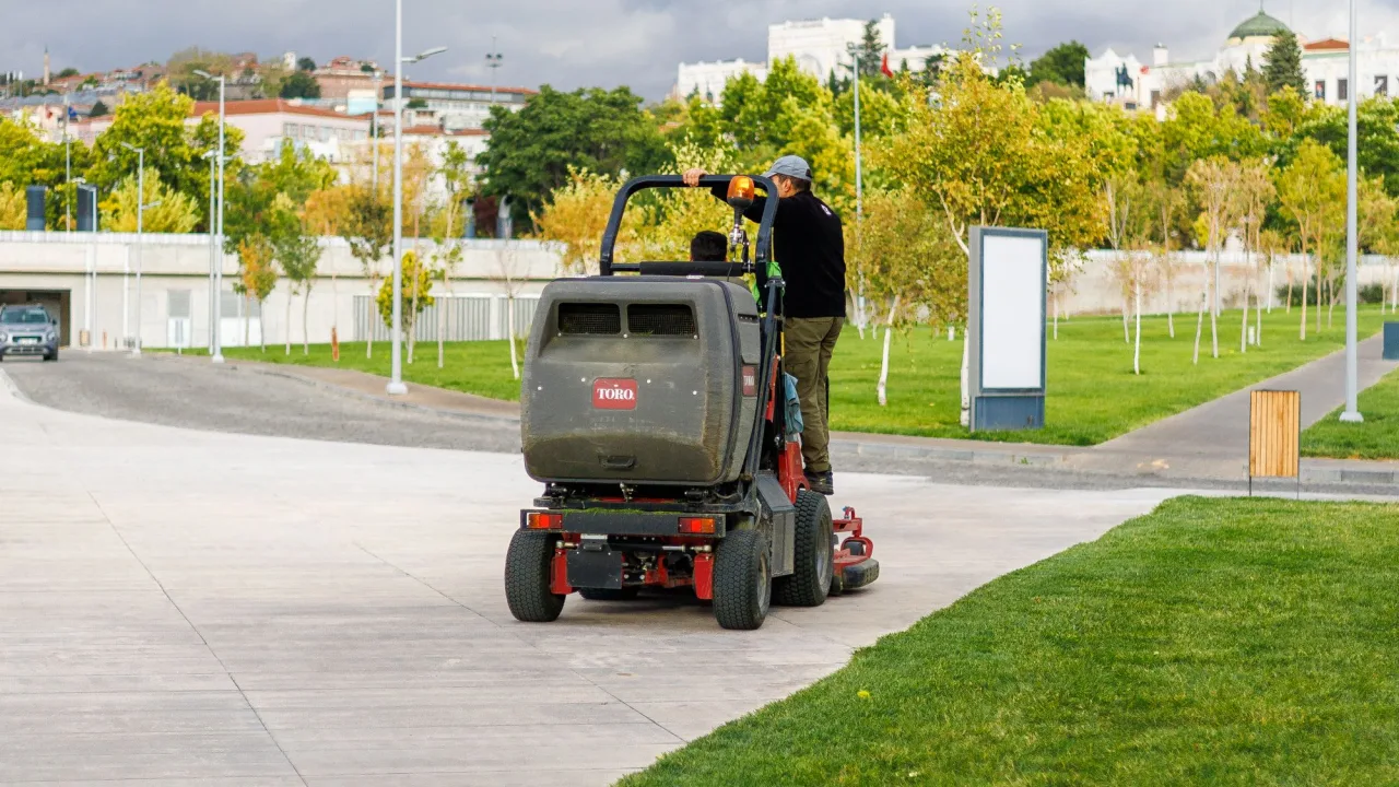 A single operator running a commercial stand-on mower along a path in a park