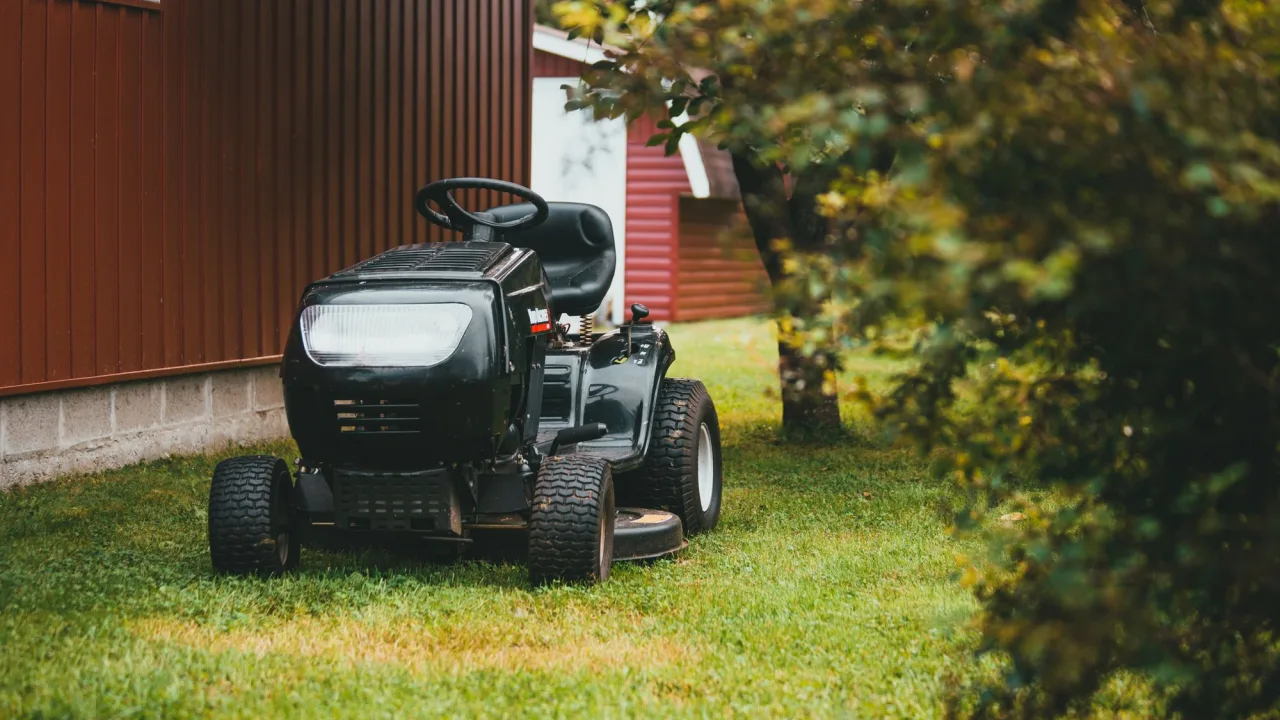 A black riding mower parked on a lawn beside a red barn