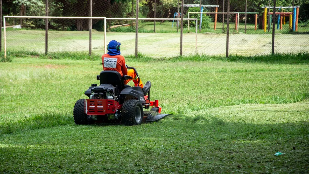 A solo lawn care operator mowing an open field on a zero-turn riding mower