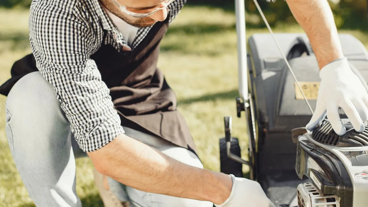 A lawn care worker in gloves and safety glasses servicing a push mower engine